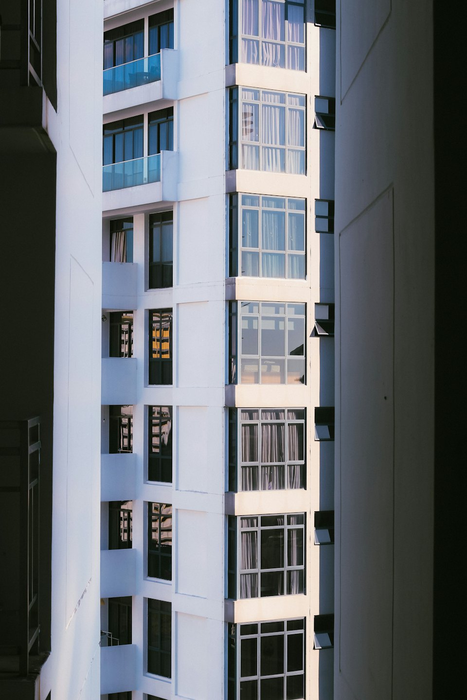 Moderno edificio in cemento bianco con grandi finestre in vetro e balconi blu.