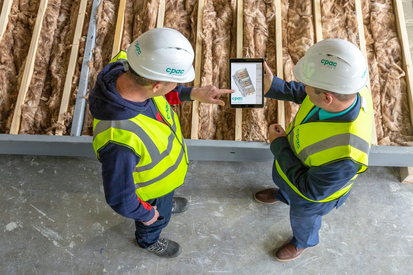 Due operai edili discutono un tablet digitale in un cantiere.